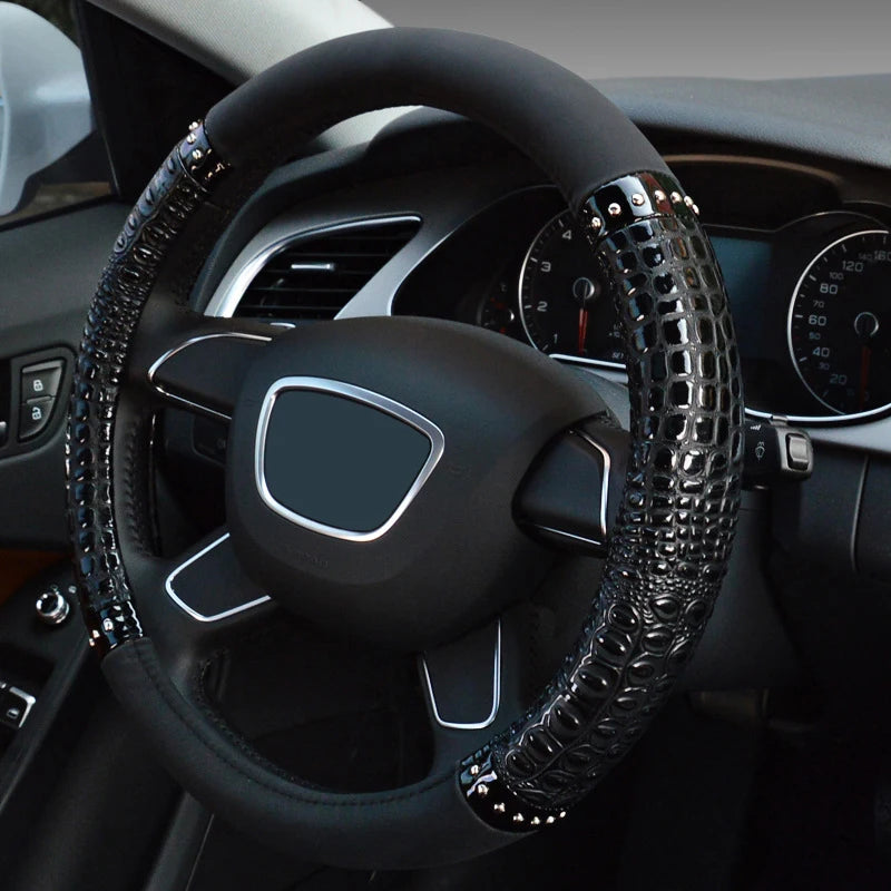 A close-up view of a black car steering wheel with crocodile grain leather cover and silver accents.