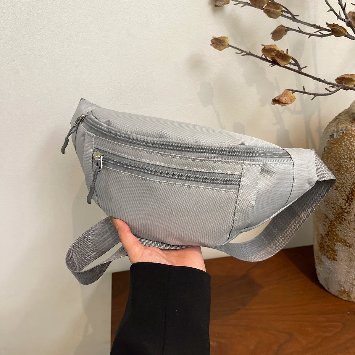 A hand holds a gray nylon crossbody waist pack against a light background.