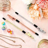 A set of gold and rose gold retractable bracelet fastening tools with black handles displayed on a pink surface.