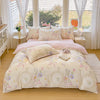 A light pink and cream printed duvet cover set with pillows displayed on a bed near a window.
