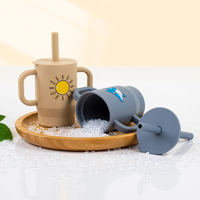 A beige silicone training cup with a straw and handles is shown next to crushed ice on a wooden board.