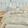 Beige besticktes Blumen-Bettwäscheset mit strukturierten weißen Kissen auf einem Bett.