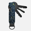 A minimalist aluminum key organizer with a dark blue and gold speckled finish, holding several keys.