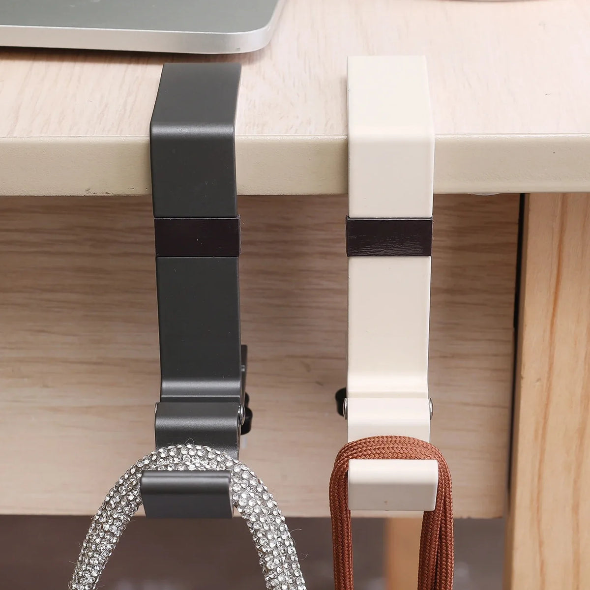A close-up of a black foldable aluminum desk hook with a silver mesh loop and a white version.