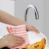 A hand wipes a kitchen faucet with a pink microfiber cloth, demonstrating how to clean oil.