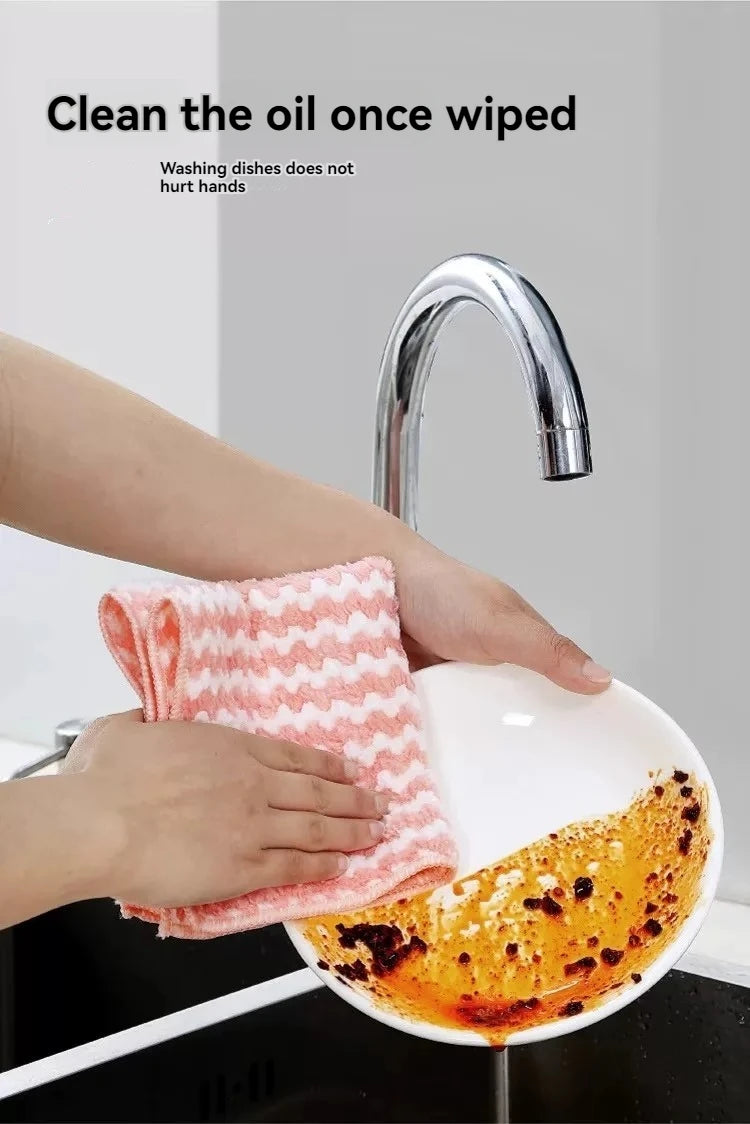 A hand wipes a kitchen faucet with a pink microfiber cloth, demonstrating how to clean oil.