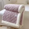 A folded double-layer fleece throw blanket in mauve and white with a quilted texture resting on a white bed.