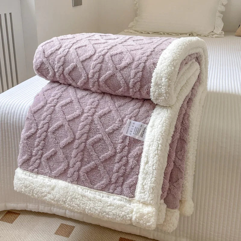 A folded double-layer fleece throw blanket in mauve and white with a quilted texture resting on a white bed.
