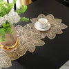 A gold-toned ceramic teacup rests on a decorative gold leaf floral pattern table runner and placemat set.