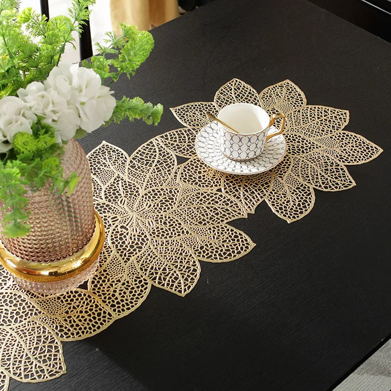 A gold-toned ceramic teacup rests on a decorative gold leaf floral pattern table runner and placemat set.