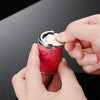 A hand is opening a red patterned metal coin tube keychain to reveal a silver coin inside.