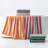 A set of soft plaid cotton bath towels in various striped colors stacked on a white surface.