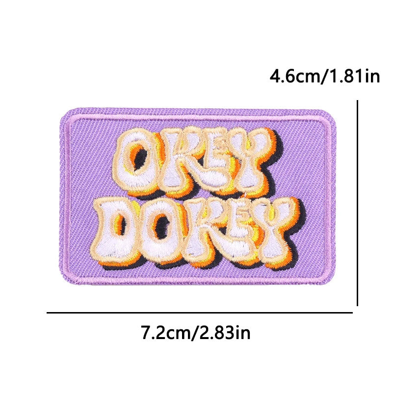 Purple embroidered iron-on patch featuring the words OKAY DOKEY in orange and yellow thread.