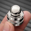A close-up of a silver metal desk spinner with a smooth ball top being held by a hand.