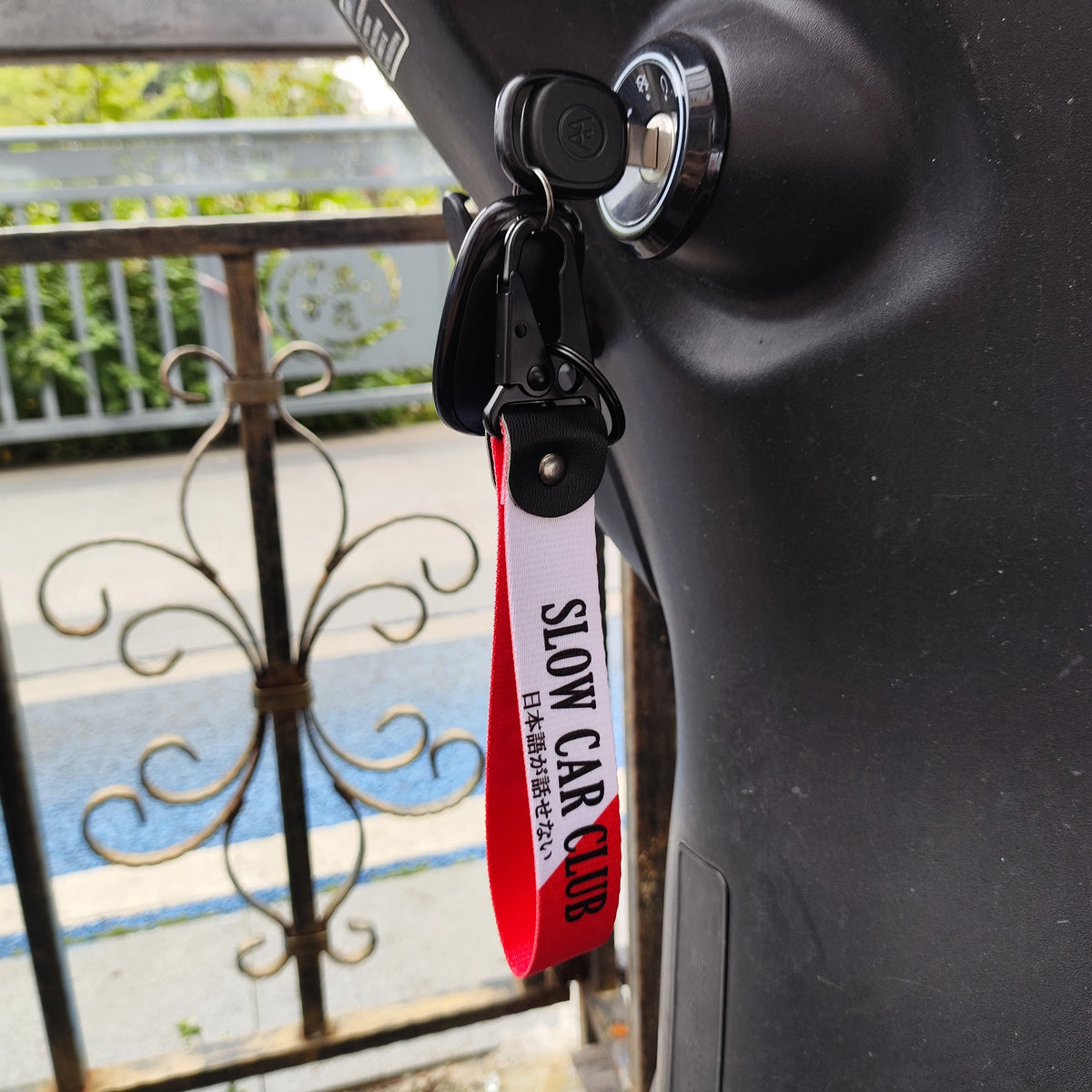A black keychain with a red tag reading SLOW CAR CLUB attached to a car door handle.