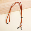 A brown leather adjustable lanyard with a black bead and silver clasp is displayed on a light wooden surface.