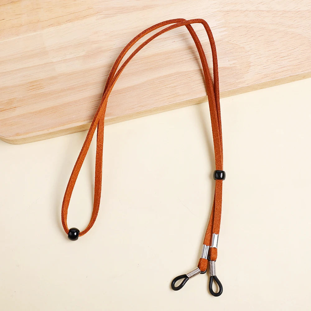 A brown leather adjustable lanyard with a black bead and silver clasp is displayed on a light wooden surface.