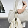 A hand is adjusting an adjustable beige luggage strap on a light-colored canvas bag.