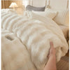 A close-up of a thick, cream-colored faux fur comforter draped over a bed.