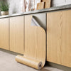 A roll of self-adhesive wood grain floor stickers is shown next to light wood cabinetry and a countertop.