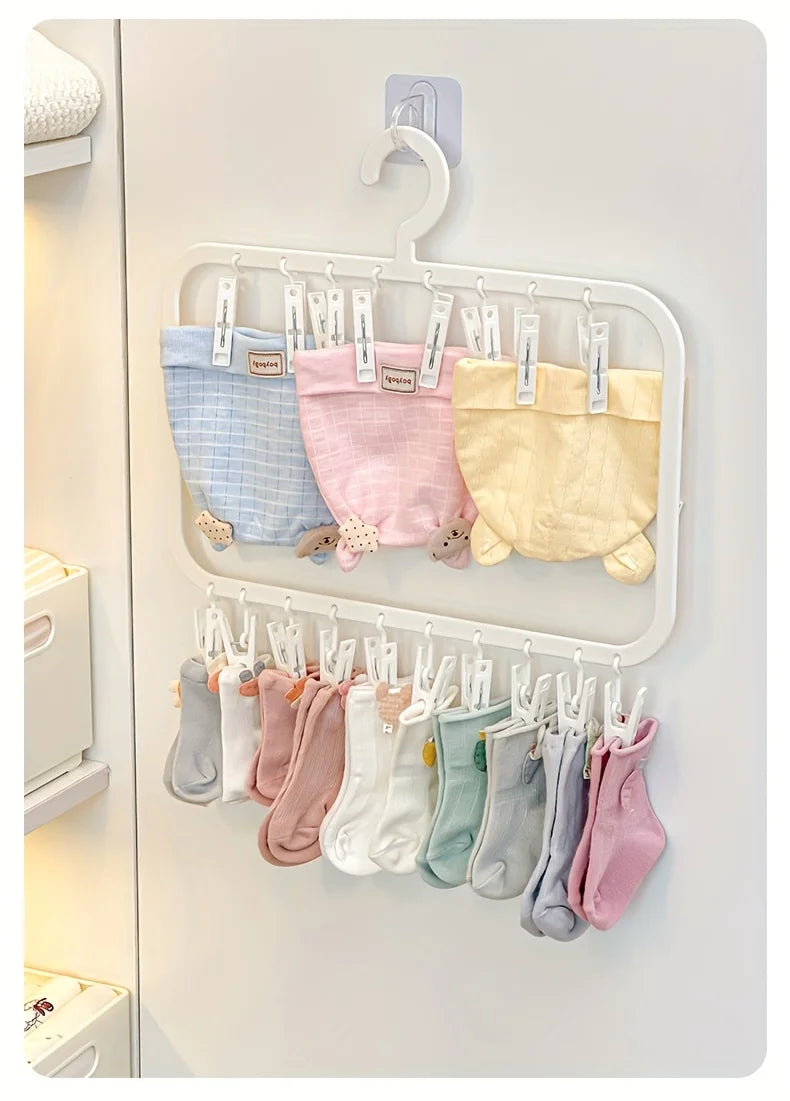 A white laundry drying rack with multiple hanging clips holding various colored baby bodysuits and tops.