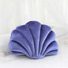 A soft lavender velvet shell print throw pillow resting on white bedding.