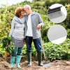 An elderly couple stands in a garden, holding hands and standing next to a shovel.