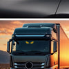 A close-up of a truck cab with a yellow demon eye LED decal on the windshield against an orange sunset background.