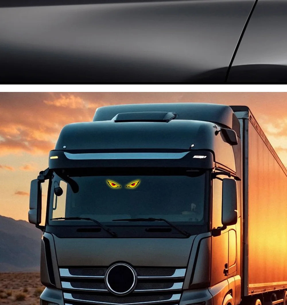 A close-up of a truck cab with a yellow demon eye LED decal on the windshield against an orange sunset background.