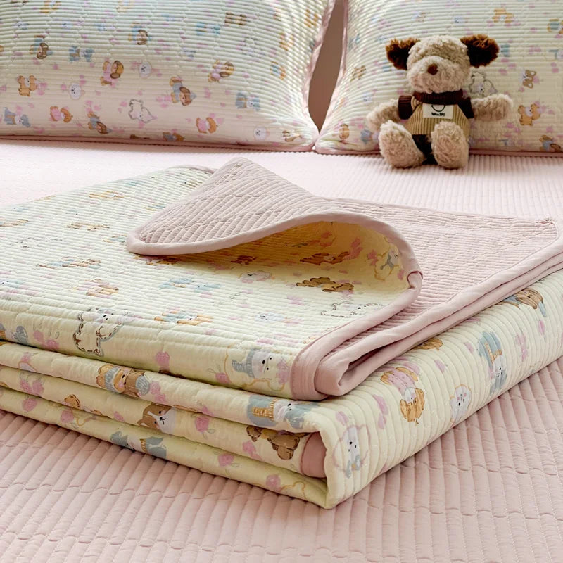 A stack of floral quilted pink and cream polyester coverlets with a teddy bear toy on a pink bed.