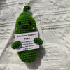 Handcrafted pickle plush with a green fuzzy body and black eyes, resting on a white textured surface.
