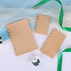 A collection of loose leaf notebook refill paper in tan and white, with a green ribbon and a small decorative item.