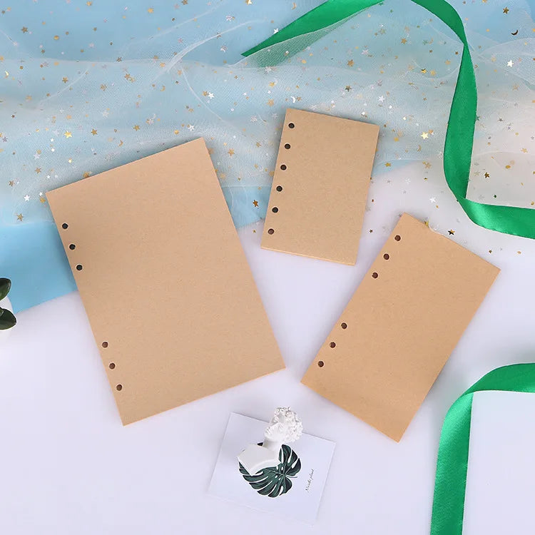 A collection of loose leaf notebook refill paper in tan and white, with a green ribbon and a small decorative item.