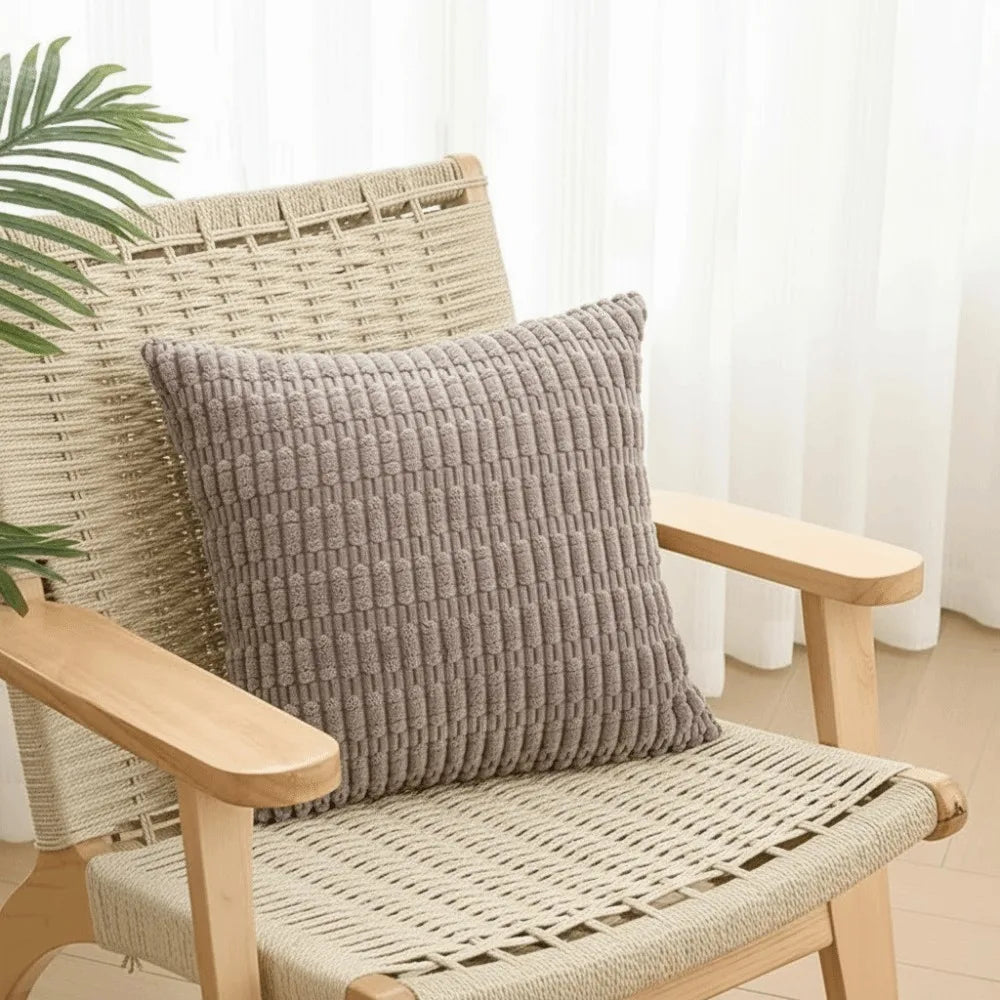 A woven wicker chair with a gray corduroy pillow and matching woven seat cushion.