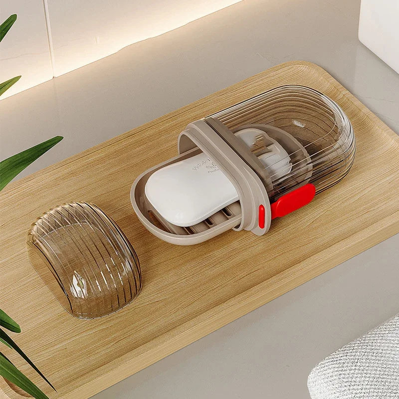A portable travel soap box with a drainage lid and a white soap bar is displayed on a wooden tray.