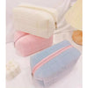 A set of three portable makeup bags in white, pink, and light blue with zippers.