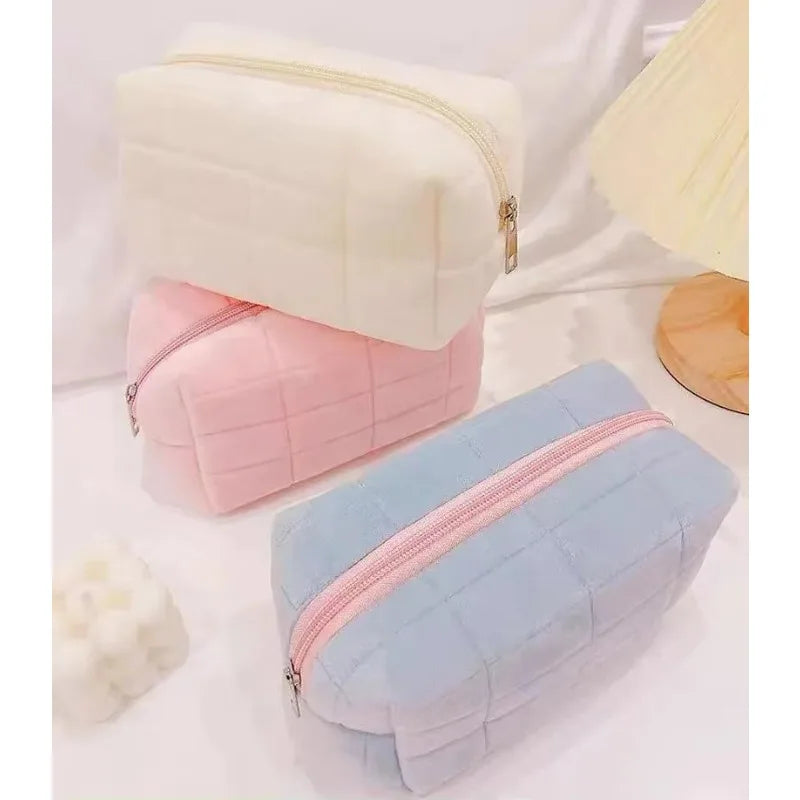 A set of three portable makeup bags in white, pink, and light blue with zippers.