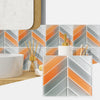 A close-up of white vessel sink and a bathroom wall tiled with orange and gray herringbone marble peel-and-stick tiles.