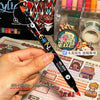 A hand holds a black dual-tip acrylic paint marker with a gold tip, demonstrating the product for art and craft.