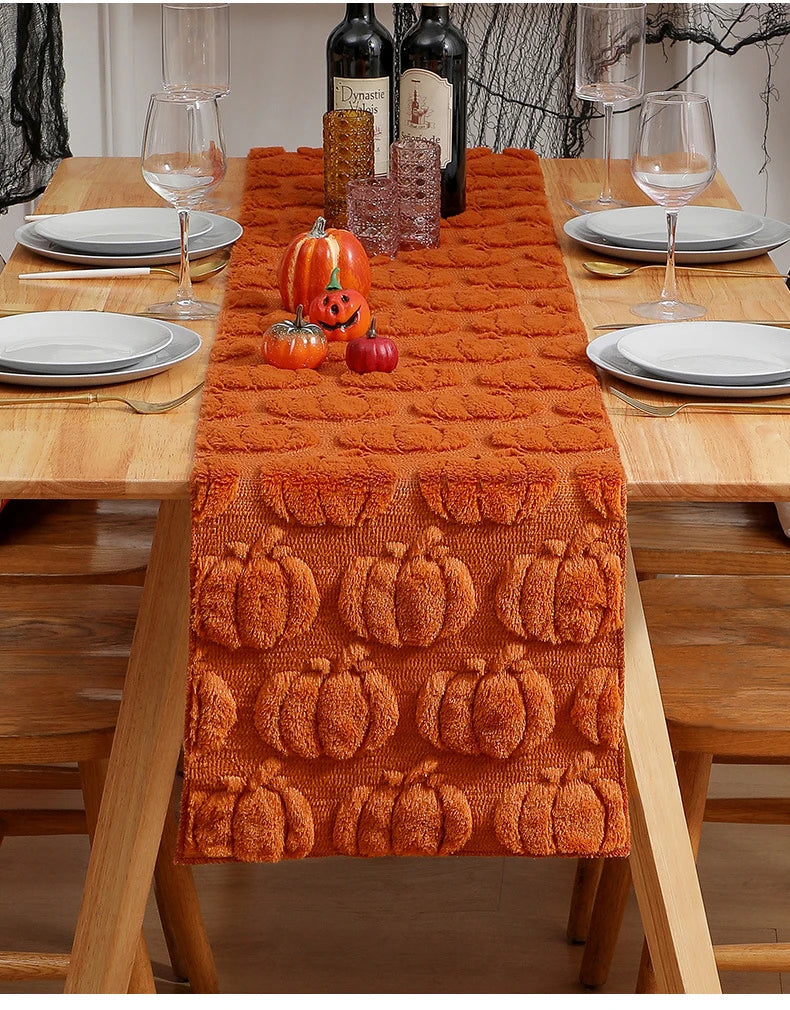 An orange textured table runner with carved pumpkin designs is displayed on a wooden table set for a holiday meal.