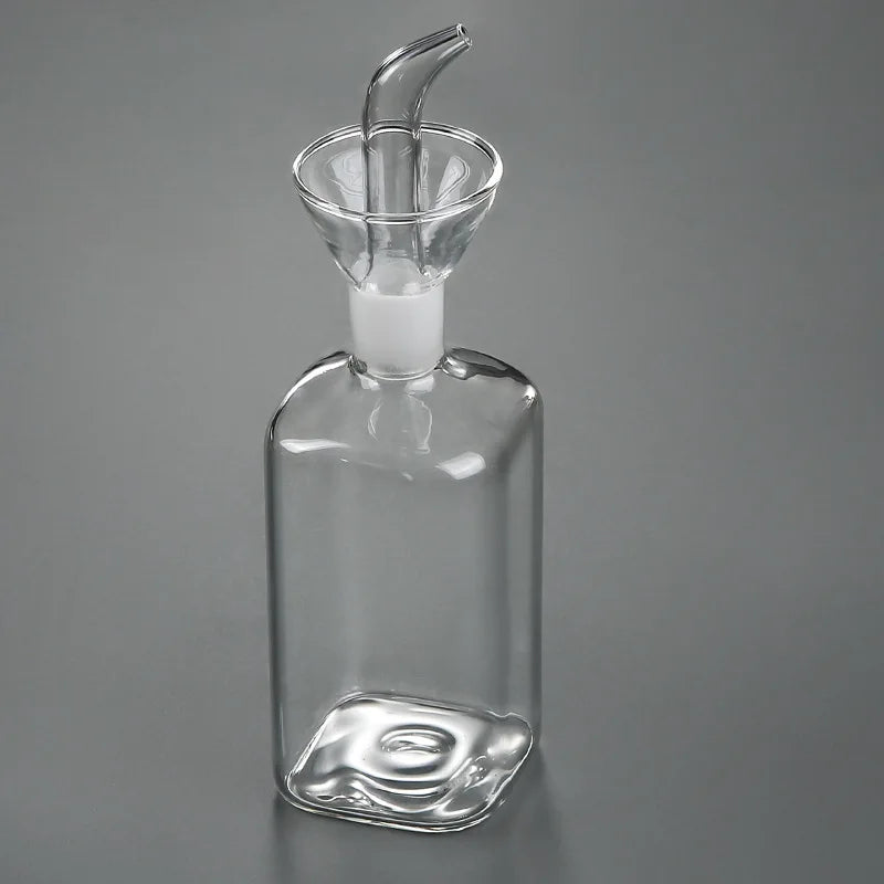 A clear borosilicate glass oil and vinegar dispenser with a glass funnel top and a white stopper.
