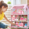 A young girl is playing with a pink dollhouse furniture set featuring miniature rooms and accessories.
