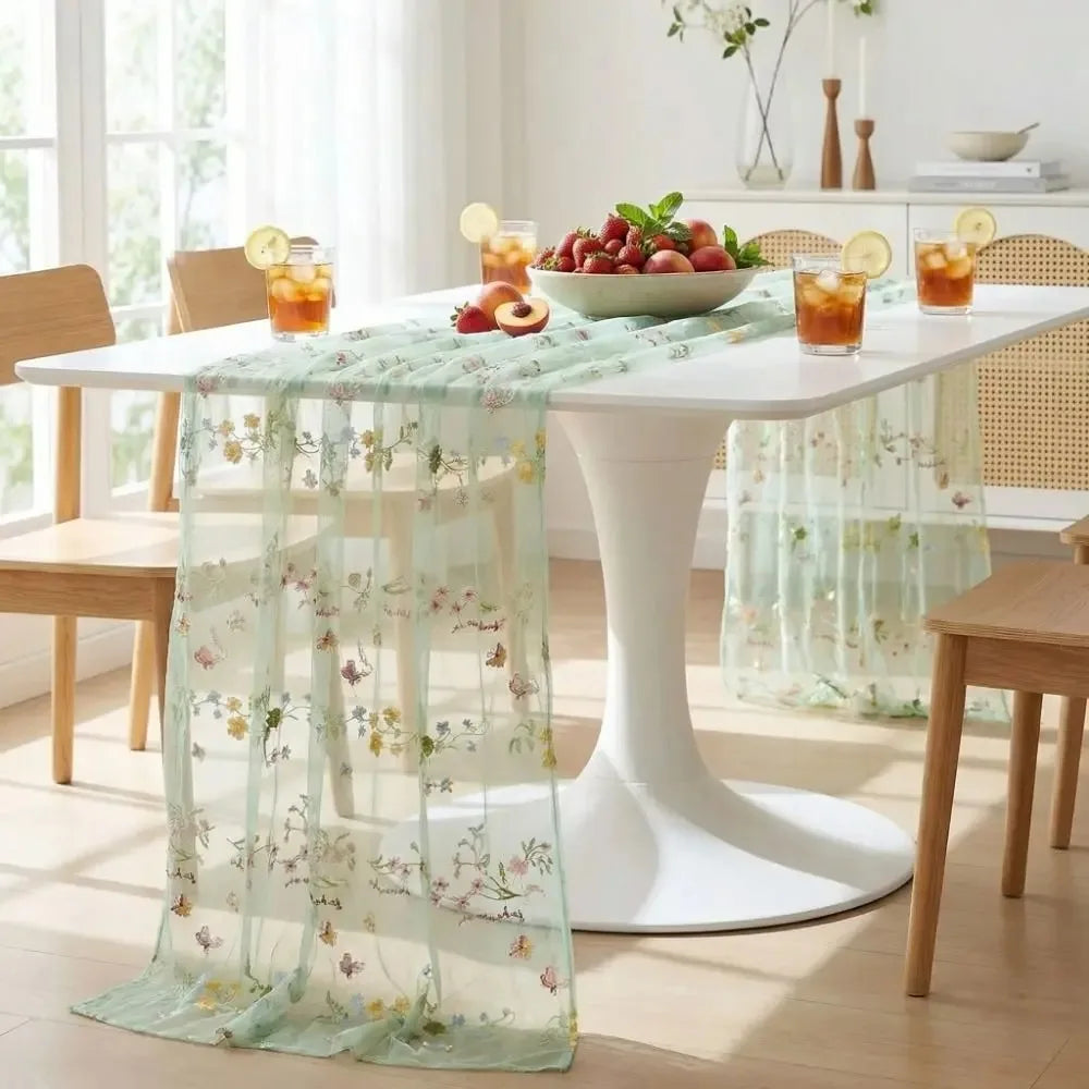 A white dining table is set with a sheer mint green tulle table runner featuring floral embroidery.