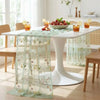 A white dining table is set with a sheer mint green tulle table runner featuring floral embroidery.