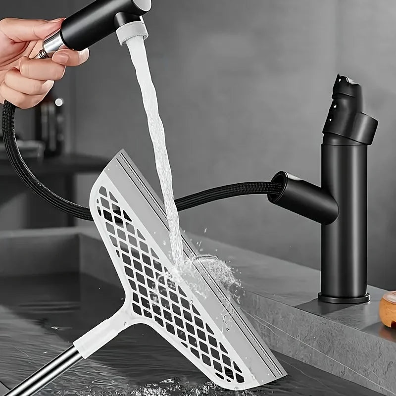 A hand is using a detachable broom with a double-sided silicone scraper to clean a surface.