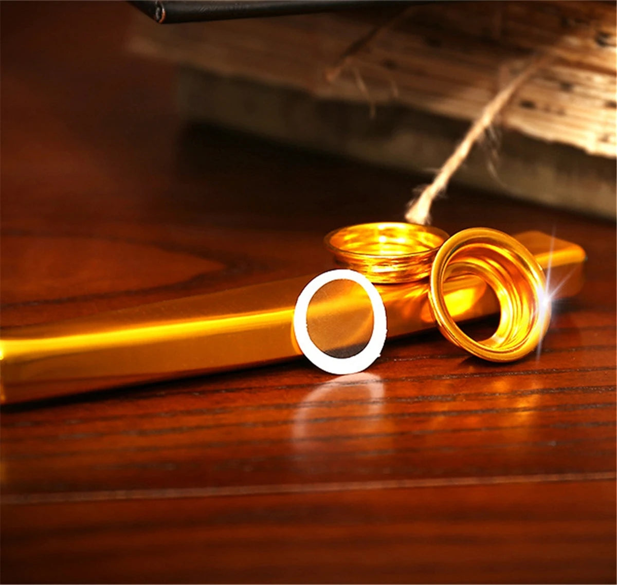 A close-up of a gold-colored aluminum kazoo with a silver membrane diaphragm resting on a wooden surface.