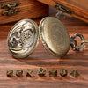 A pair of antique brass dragon-themed pocket watch dice cases with seven metal polyhedral dice resting on dark wood.
