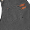 A dark gray cotton canvas apron featuring a chest pocket and two leather cross-back straps.