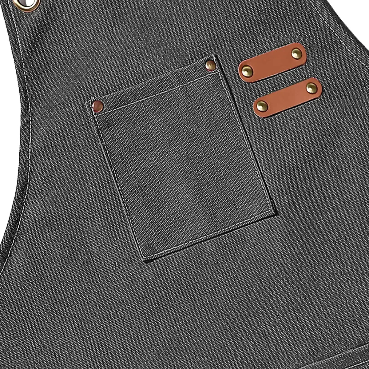 A dark gray cotton canvas apron featuring a chest pocket and two leather cross-back straps.