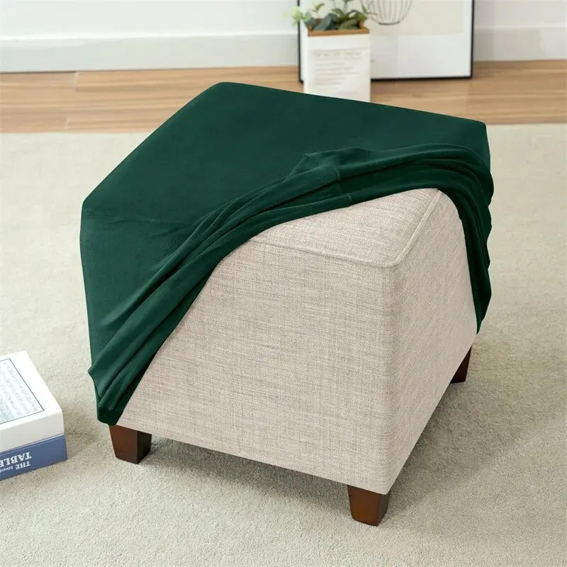 A dark green stretch velvet slipcover draped over a light beige square ottoman or pouf.